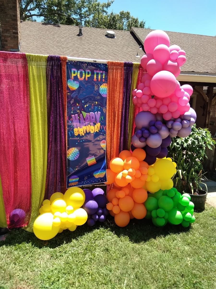 Pop It birthday backdrop with rainbow sequin curtains and a pink, purple, orange and green garland