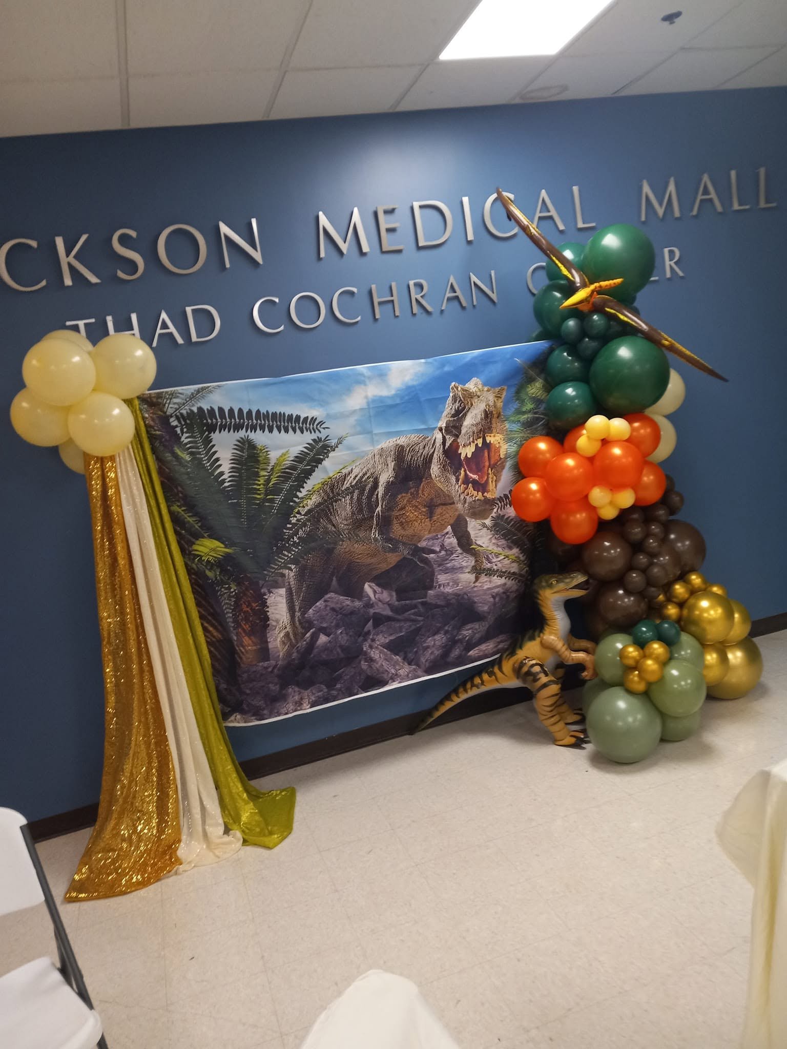 Dinosaur birthday backdrop with a green, orange, brown and gold balloon garland